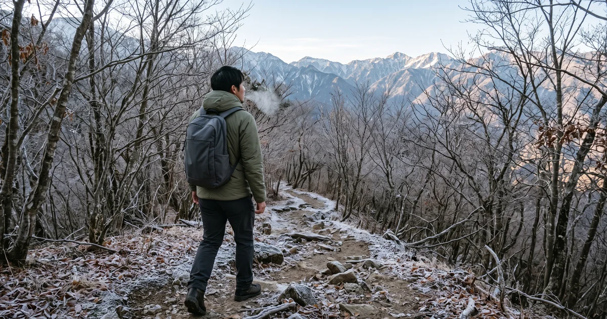 霜の降りた晩秋の登山道を、中綿入りのフード付きジャケットを着て歩く登山者の後ろ姿