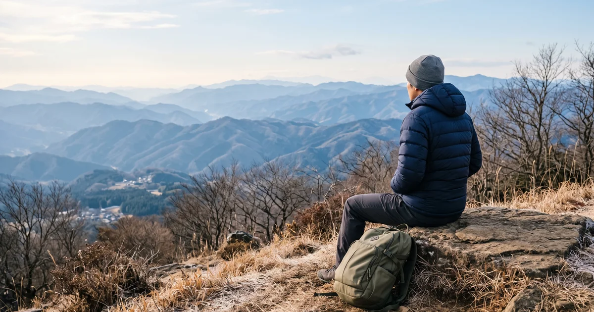 冬の低山の山頂で、ダウンジャケットを羽織って休憩する登山者