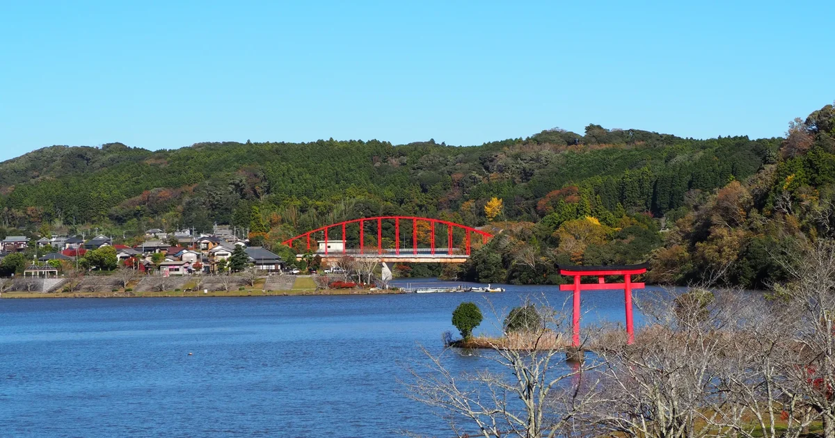 秋の亀山湖。湖面に立つ赤い鳥居と紅葉の丘陵