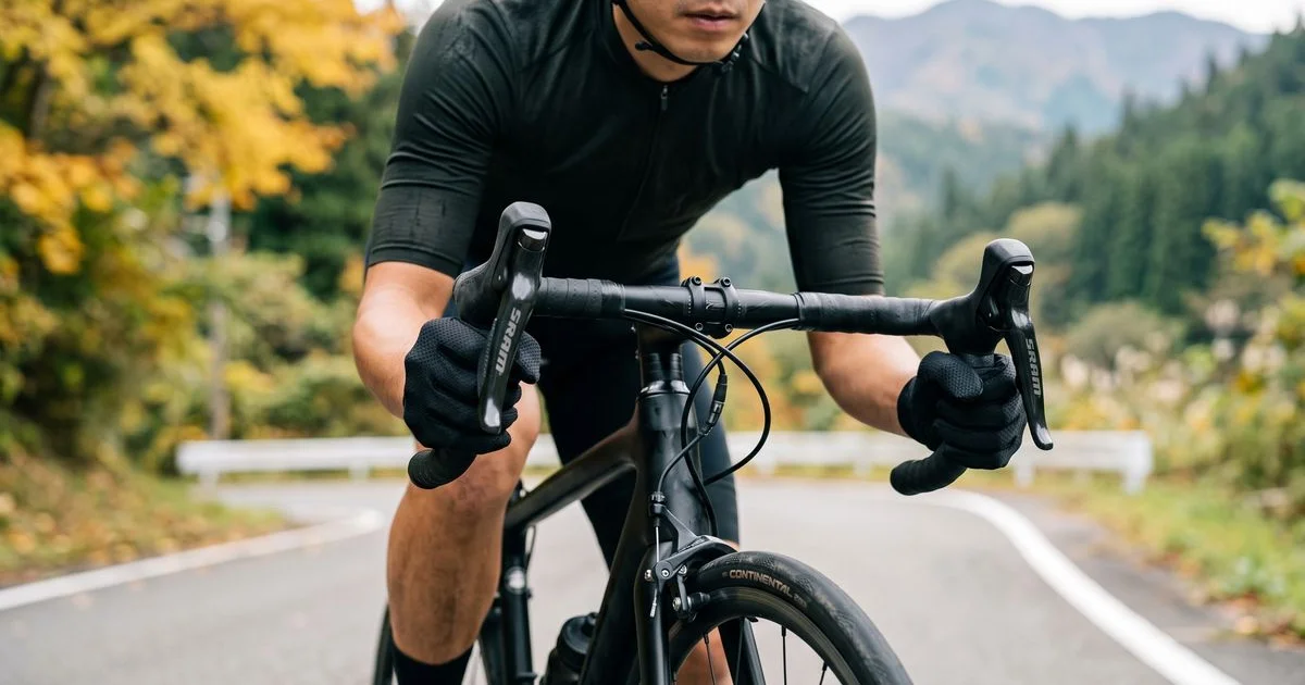春秋の道をロードバイクで走るサイクリストの、薄手フルフィンガーグローブでハンドルを握る手元